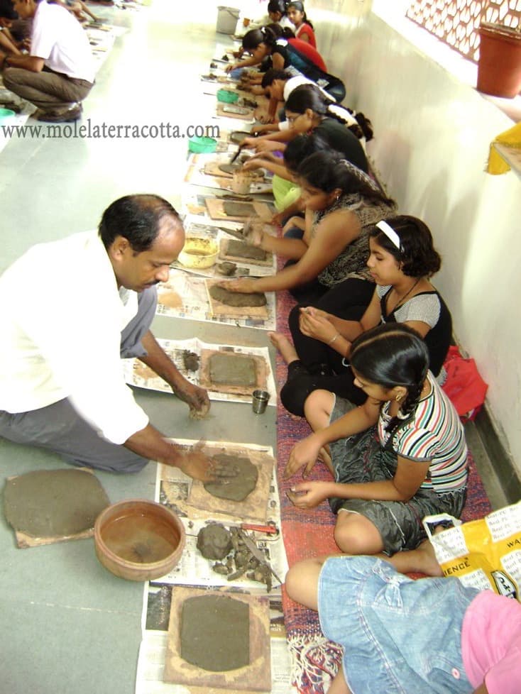 Dinesh Chandra Kumhar demonstrating relief work to a row of students seated along the workshop floor