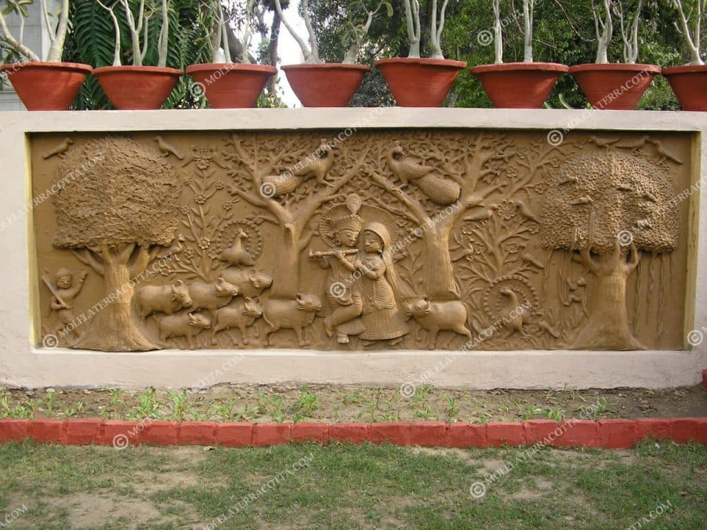 Terracotta relief mural of Krishna and Radha with cows, trees, and peacocks built into a garden wall