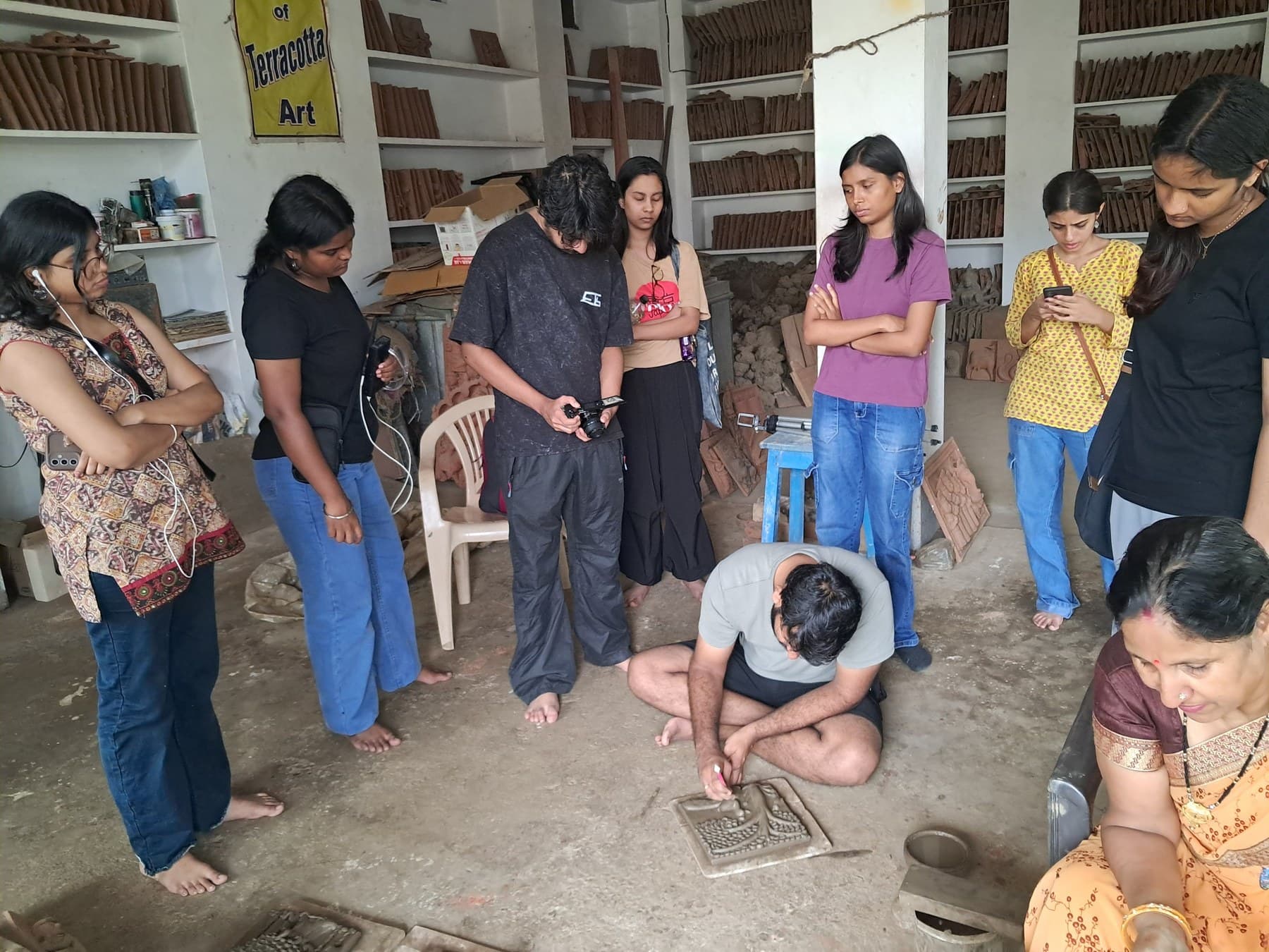 Dinesh Chandra Kumhar demonstrating terracotta relief sculpting to students seated in the Molela workshop