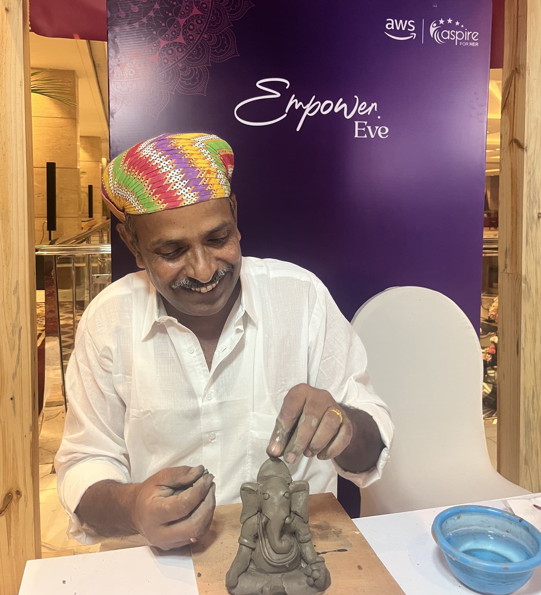 Dinesh Chandra Kumhar hand-sculpting a clay Ganesha idol during a live demonstration in traditional Rajasthani attire