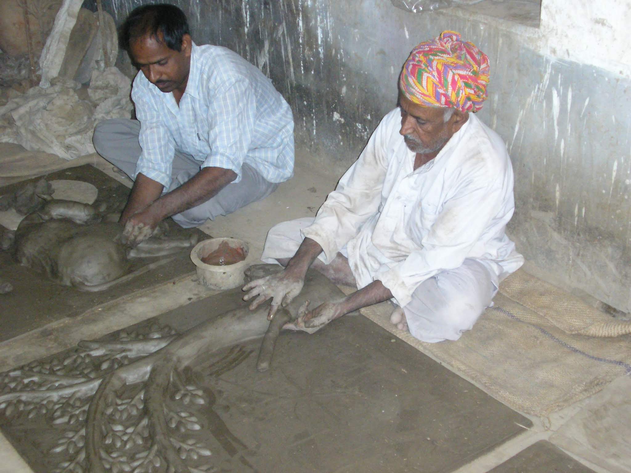Dinesh Chandra Kumhar sculpting terracotta relief murals on the workshop floor beside Padma Shri Mohan Lal Kumhar