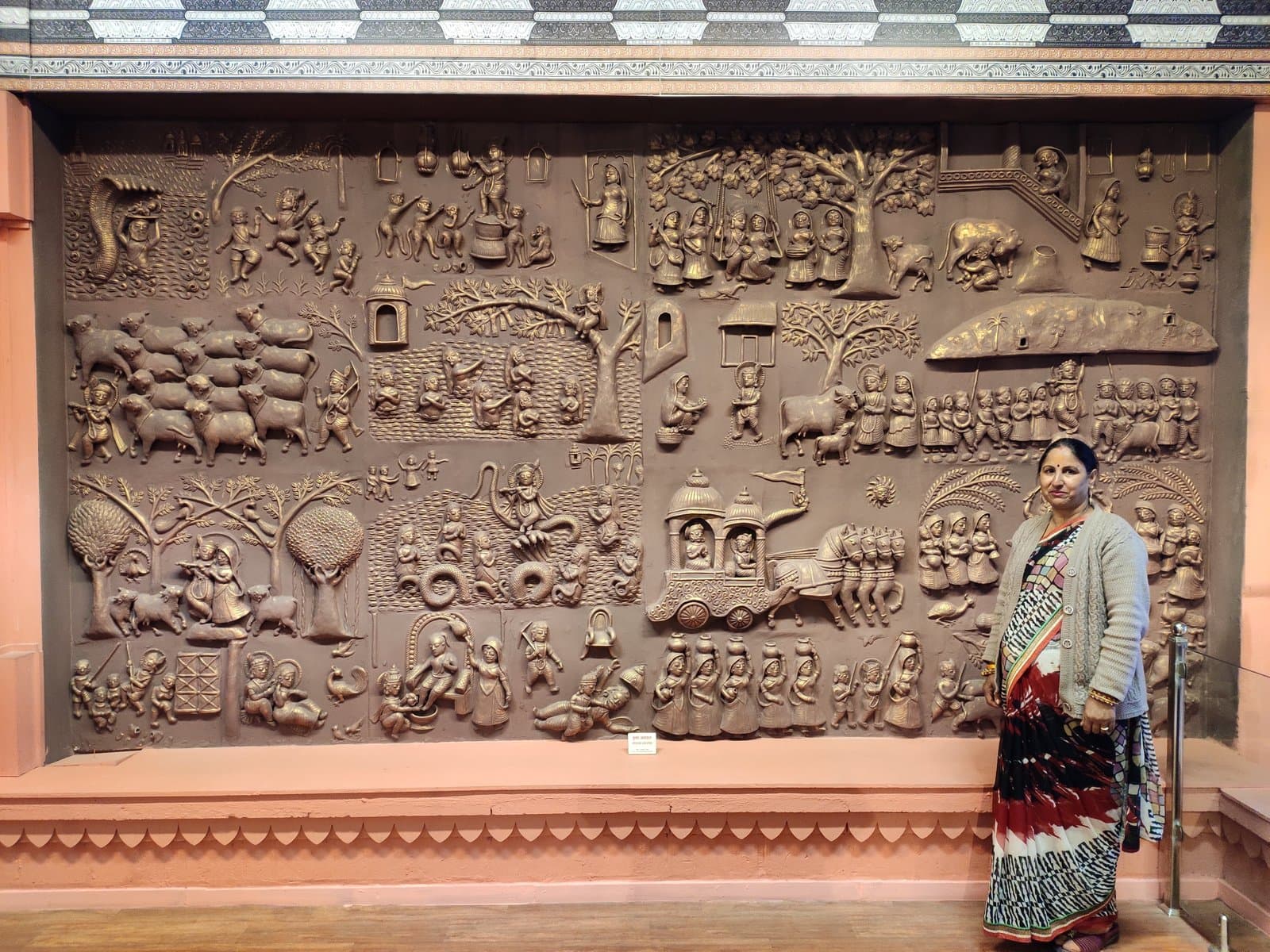 Kailash Devi standing beside the monumental Krishna Leela terracotta wall mural