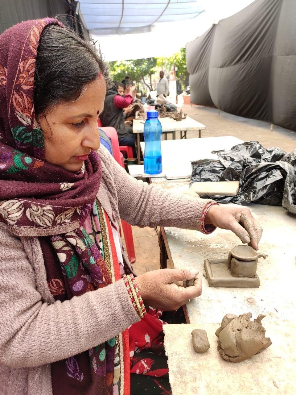 Kailash Devi hand-modelling a sacred terracotta Shiva lingam and votive shrine at a live craft workshop