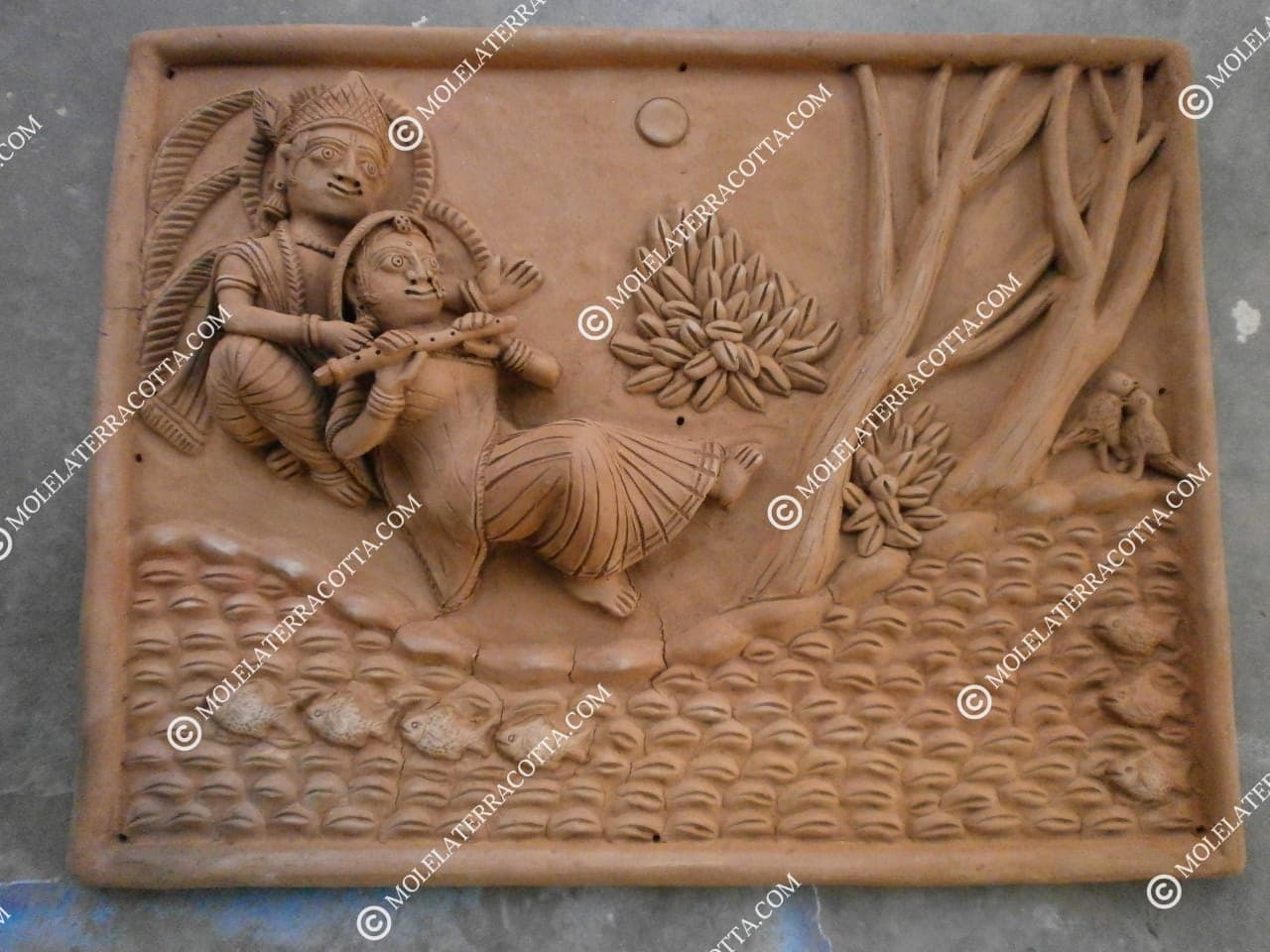 Terracotta wall decor tile showing Radha and Krishna playing flute by the river